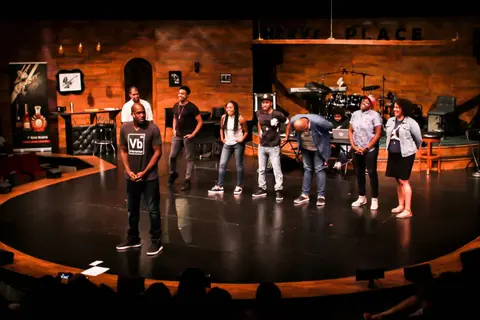 Performers stand in a line on a round theatre stage.