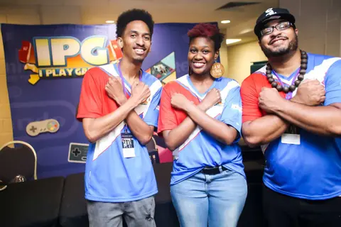 Three people in game jerseys cross their arms in front of a gaming booth.