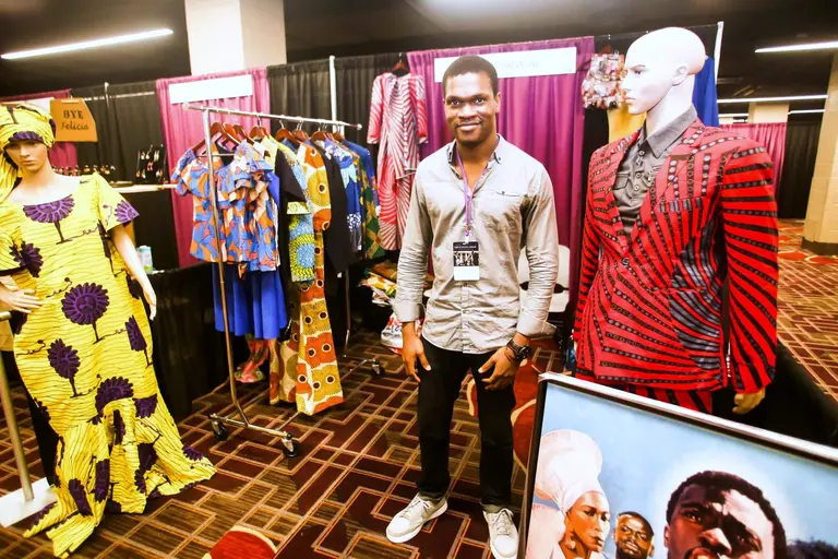 A young man stands between two mannequins dressed in yellow and red wax-print outfits.