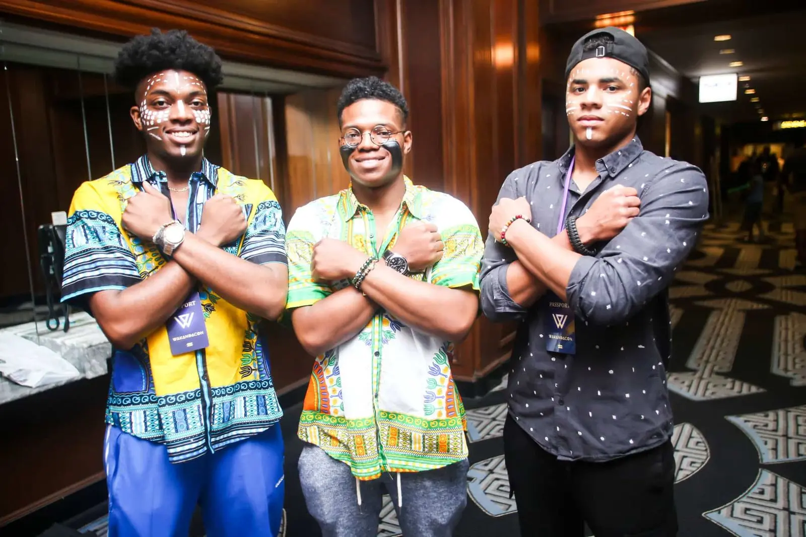 Three young men in dashikis and print shirts cross their arms and grin.