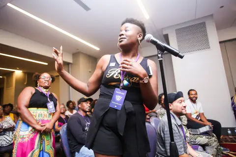 A woman in the audience stands at a microphone and gestures as she asks a question.