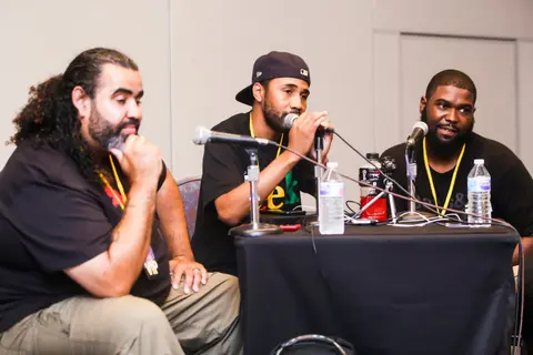 Three men sit at a panel table with microphones and water bottles.