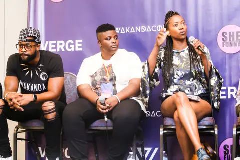 Three panelists sit in front of the purple backdrop with a pink She Funny logo.