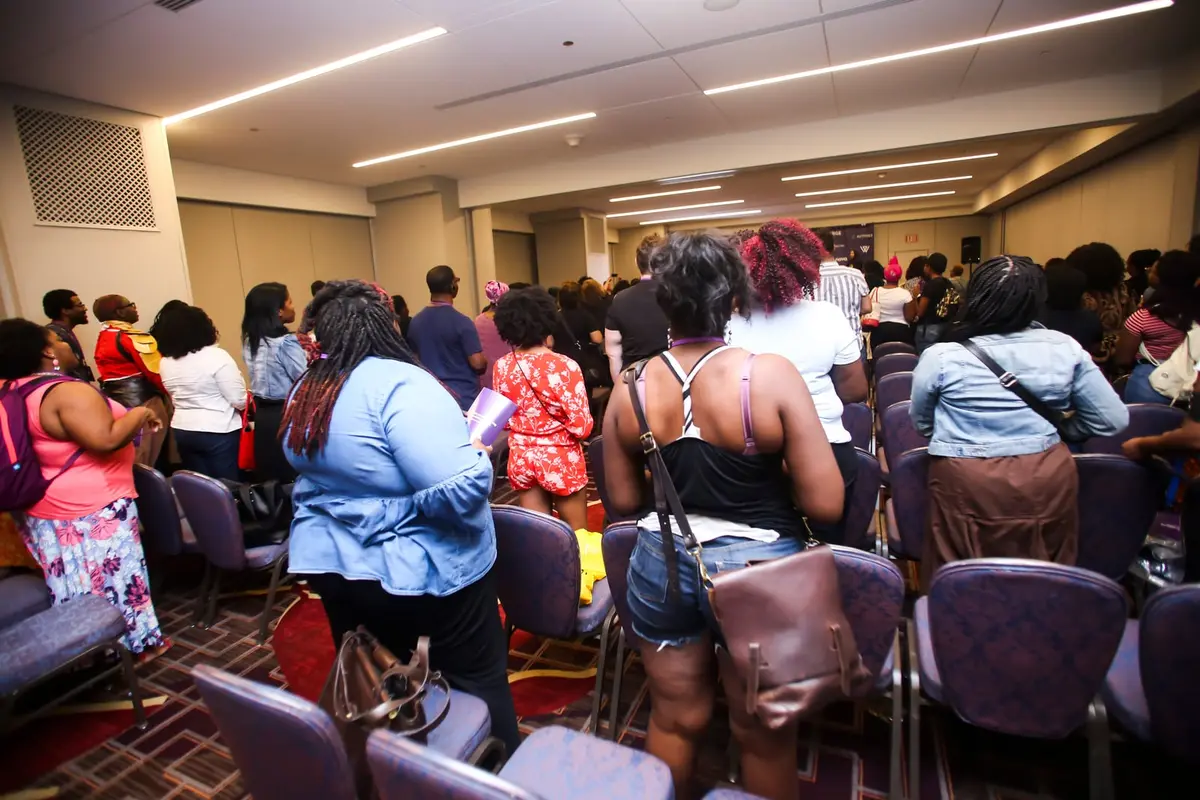 A crowd stands and sits through a hotel meeting room during a session.