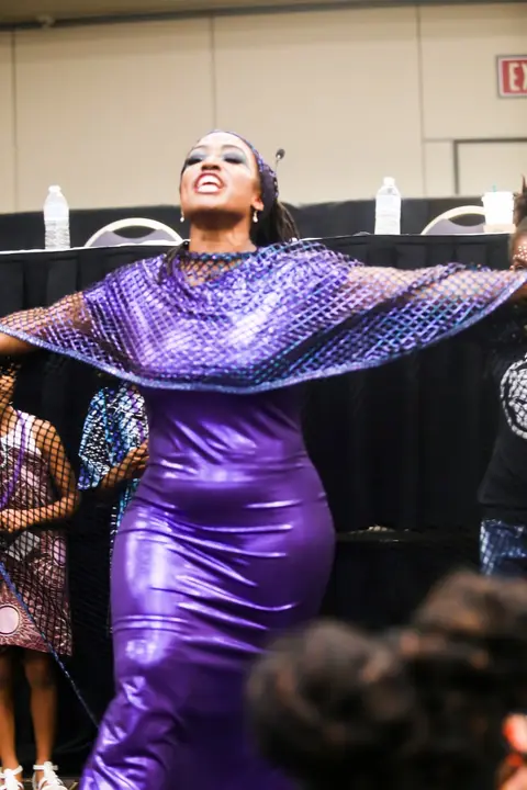 A woman in a shimmering purple gown spreads her cape wide.