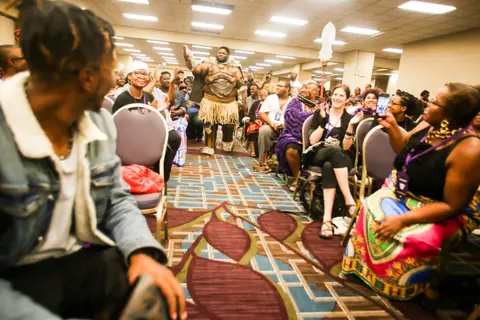 Attendees turn in their seats as a cosplayer in armour walks the aisle.