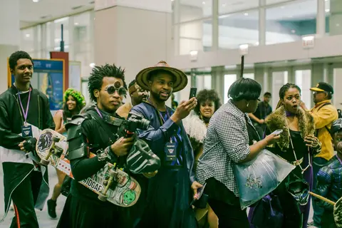 A crowd in costume, with phones raised, fills the concourse under tall windows.