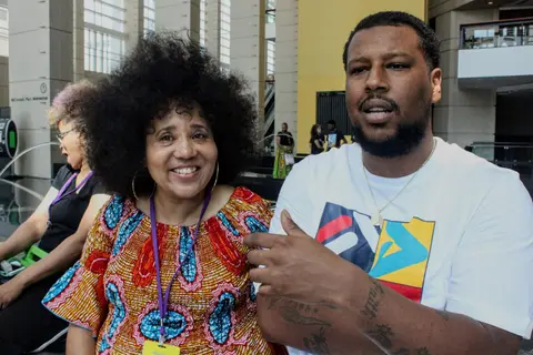A woman with a full natural and a print dress smiles beside a man talking with his hands.