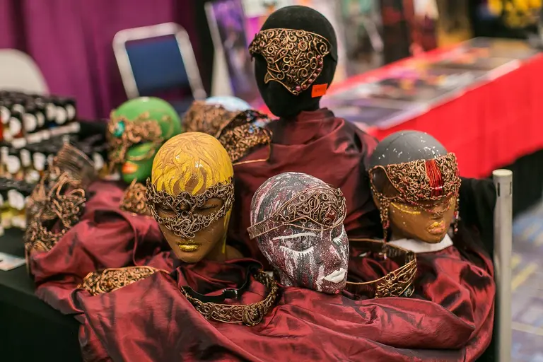 Five decorated masks in gold, silver and bronze rest on stands over deep red cloth.