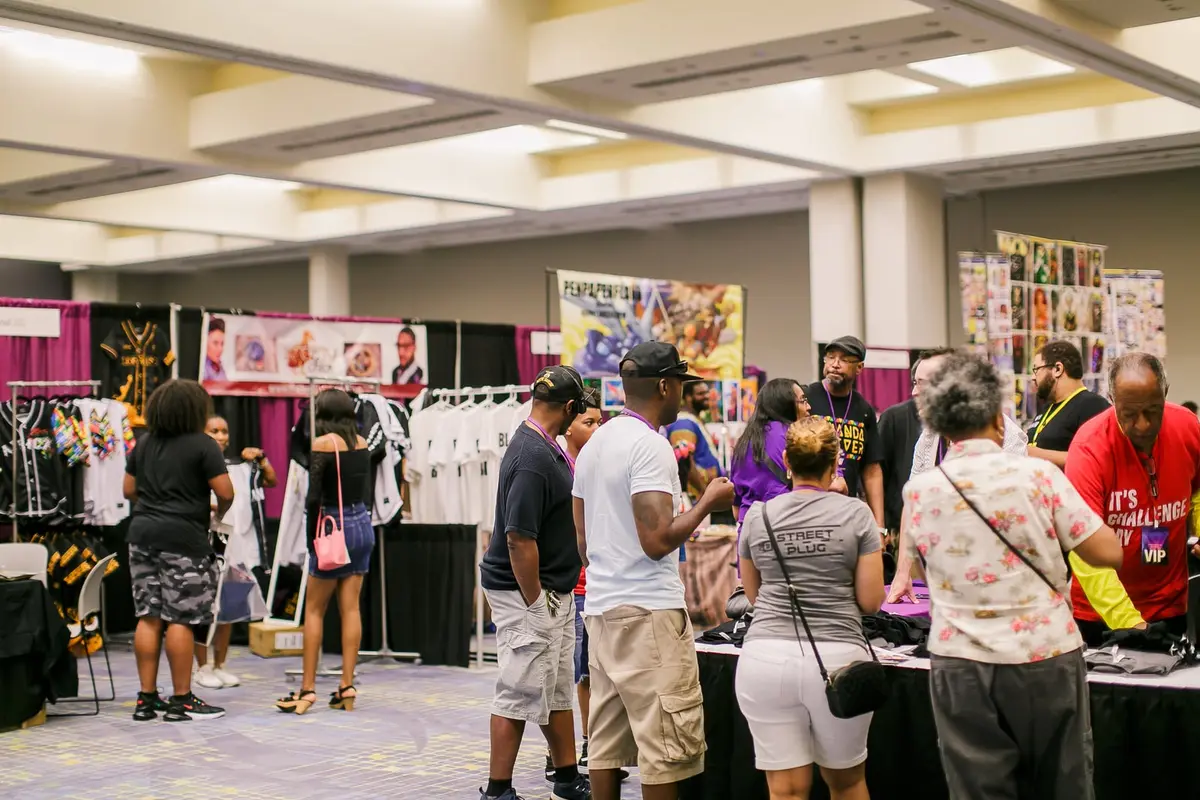 A crowd of shoppers fills the aisles between vendor booths with purple drapes.