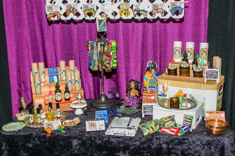 A table of bottles, jars and print fabrics under purple drapes.