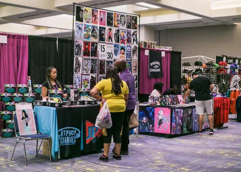 Shoppers stand at booths under a tall wall of comic prints.