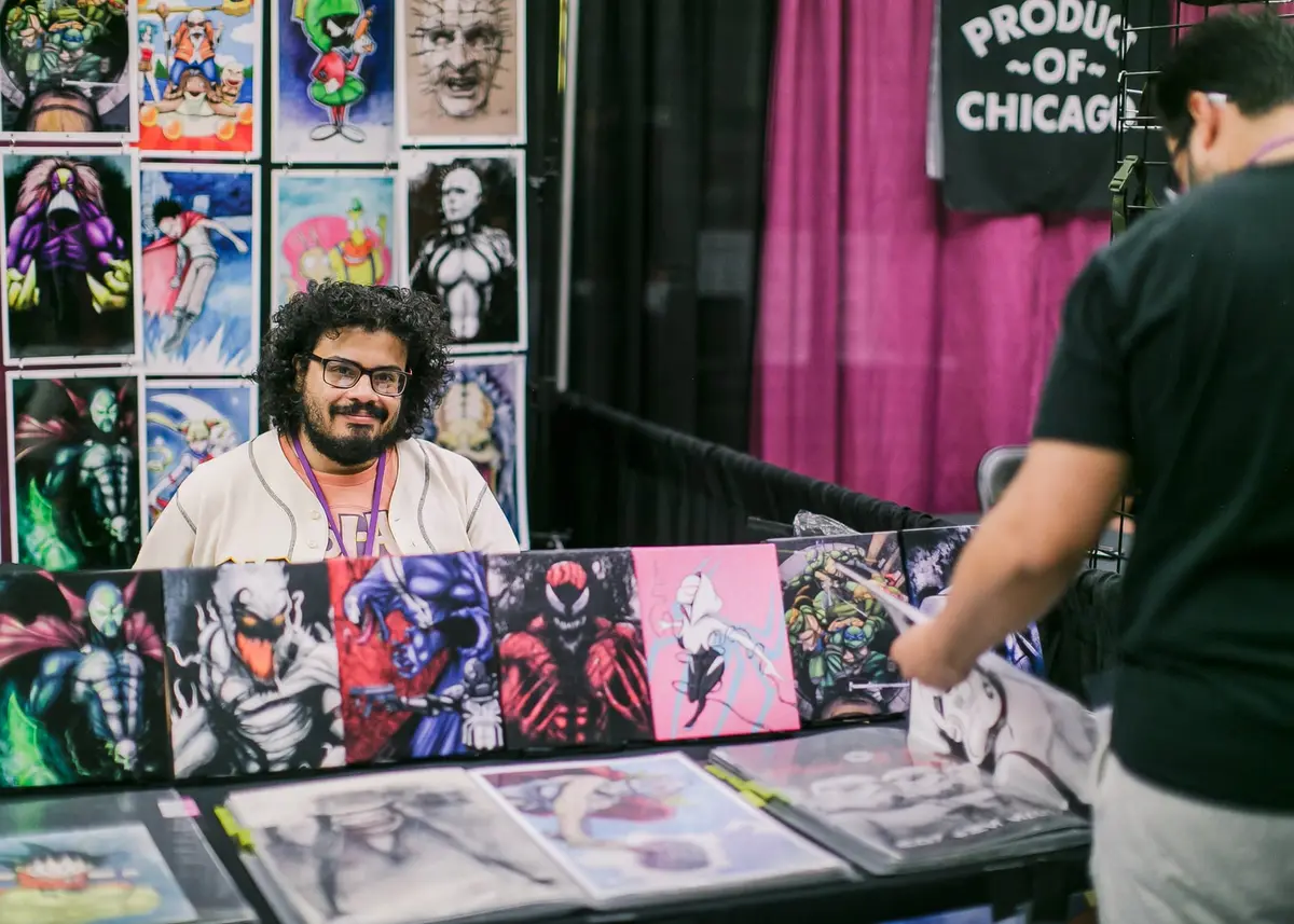 A man with curly hair sits behind a table of superhero prints.