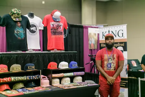 A vendor stands beside his display of caps and T-shirts.