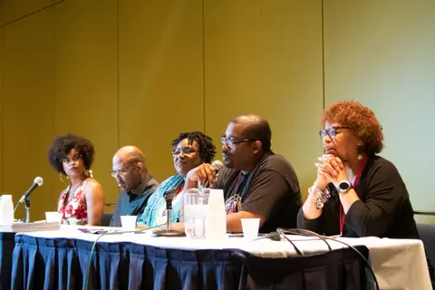 Five panelists sit at a draped table with microphones and water glasses.