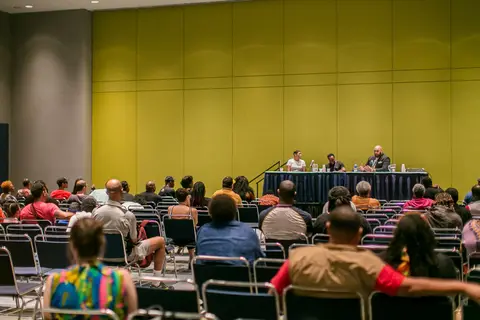 A wide view of a convention room filled with attendees facing a panel.